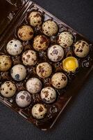 Raw quail eggs in a plastic box on a dark concrete background photo