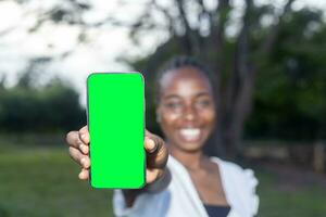 Attractive dark skinned african young woman recommending new mobile application, collage, showing green screen isolated over white background photo