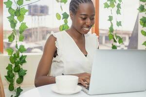 Portrait of a happy young african woman relaxing in outdoor cafe and using a laptop. photo