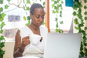 Portrait of a happy young african woman relaxing in outdoor cafe and using a laptop. photo