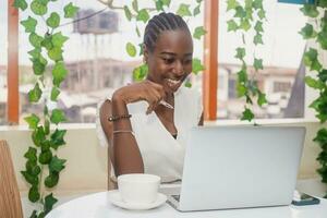 Portrait of a happy young african woman relaxing in outdoor cafe and using a laptop. photo