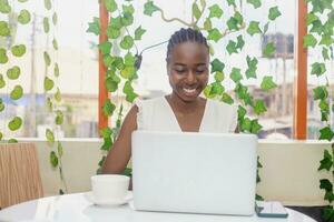 Portrait of a happy young african woman relaxing in outdoor cafe and using a laptop photo