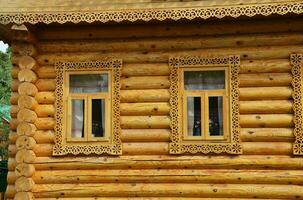 Wooden log village house. Two windows with carved patterned frames of a brown wooden house. photo