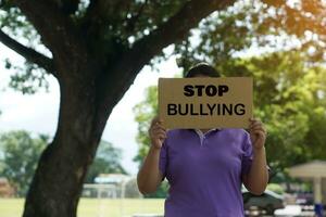 A woman holds paper placard with text Stop Bullying, outdoor background.  Concept, campaign for calling everybody to stop bullying each other by using bad word, action, texting or online. photo