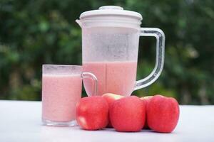 Pink apple fruits smoothie in glass and blender, outdoor background.Concept, healthy beverage for health. Well being and weight loss menu. Homemade refreshing fruit drinks. High fibers, detox. photo