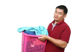 Asian man holds laundry basket full of clothes for washing, feeling lazy and bored, isolated on white background. concept, daily chores, household. Real life duty routine, washing cloth for hygiene. photo