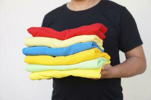 Close up man holds stack of colorful folded clothes after doing laundry. Concept, daily chore, household. Folded clothes for neat and clean. Maintenance and keep garments for sanitary. photo