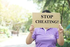 Woman protester holds paper placard with text Stop Cheating, outdoor background. Concept, campaign for stop all types of corruption or cheating. Protest for fair. Anti-bribery photo