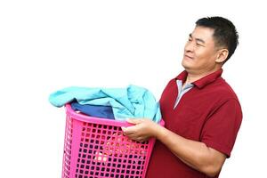 Asian man holds laundry basket full of clothes for washing, isolated on white background. concept, daily chores, household. Real life duty routine, washing cloth for hygiene. photo