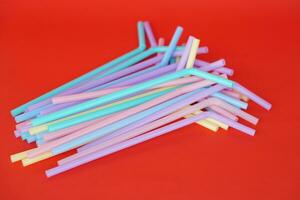 Colorful plastic drinking straws tubes for juice and cocktails, red background. Concept, single use equipment for drinking, but can use for diy crafts for decoration. photo