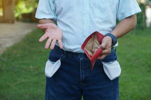 Close up man show empty money wallet and empty jeans pockets. Outdoor background. Concept, poverty. No money, poor, bad economic crisis. Financial problems. Broke or less money at the end of month. photo