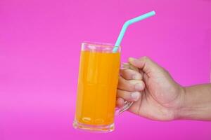 Close up of man hand holding glass of orange juice with drinking straw, on pink background. Concept, morning refreshing beverage. Sweet, testy and high vitamin C. photo