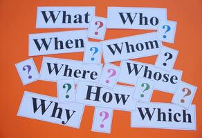 Paper cards with Wh-question words and question marks on orange background. Concept. Teaching aid. Education materials for teach WH- question. Asking questions. Suspicious symbol to find answer. photo