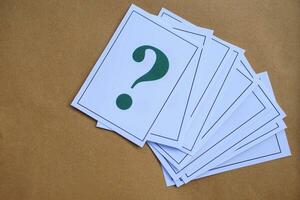 Overlapped pile of paper cards of green question mark on brown background. Concept. Teaching aid. Education materials for doing activity or playing games about find answers. photo