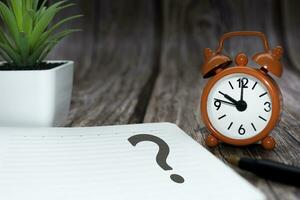 Question mark on notepad alarm clock set at 10 oclock on wooden background. photo