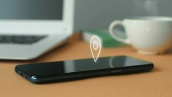 Animation of GPS geolocation icon on smartphone display against laptop and coffee cup background in office. video