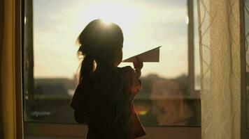 A child plays with a paper plane near the window of the house during sunset.Authentic scene. video