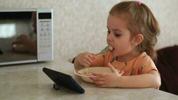 un' 3 anno vecchio bambino mangia e orologi cartoni animati utilizzando un' smartphone. cattivo abitudini. autentico scena. video