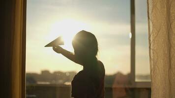 A child plays with a paper plane near the window of the house during sunset.Authentic scene. video