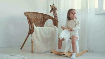 Cheerful happy girl 2 years old is swinging on a toy horse at home. video