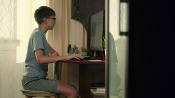 uma Garoto resolve interativo exercícios usando uma computador às casa enquanto sentado às uma mesa video