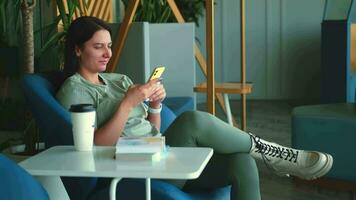 Business woman in casual clothes writes a message using a mobile phone while sitting in a modern space. video