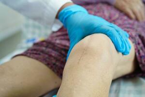 Doctor checking Asian elderly woman patient with scar knee replacement surgery in hospital. photo