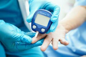 asiático médico utilizando digital glucosa metro para cheque muestra sangre azúcar nivel a tratamiento diabetes. foto