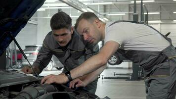 Auto mechanics discuss broken car at their garage looking under the hood video