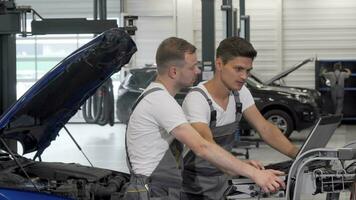 Two mechanics doing computer diagnostics of a broken car video