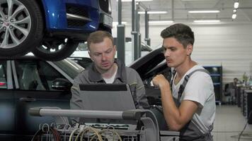 dois auto mecânica falando às a garagem usando computador portátil dentro carro diagnóstico video