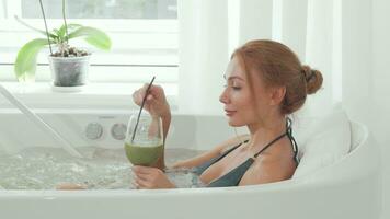 Charming woman drinking detox smoothie sitting in whirl pool bath video