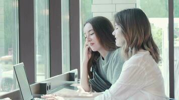 Two young women studying together at campus cafe using laptop video