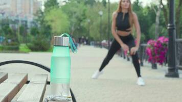 Water bottle on the foreground fit woman stretching outdoors on the back video