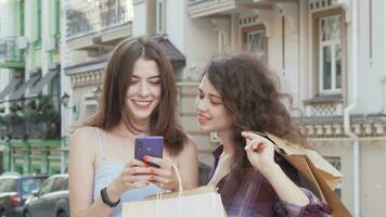 twee vrolijk jong Dames browsen online Aan slim telefoon buitenshuis video