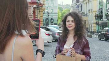 Cheerful young woman with shopping bags posing for a photo for her friend video