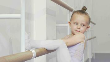 Adorable little ballerina girl putting her leg on ballet bar for stretching video