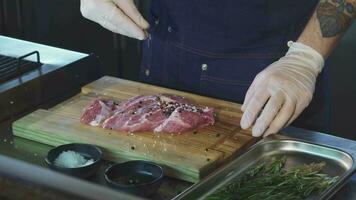 bijgesneden schot van een chef toevoegen zout Aan varkensvlees vlees voordat Koken steak video