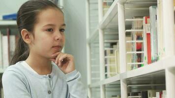 prety pequeno menina sorridente para a Câmera colheita livros às a biblioteca video