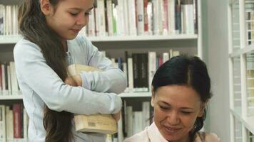 bonito pequeño niña sonriente mientras su mamá leyendo un libro a el biblioteca video