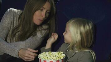 adorável pequeno menina alimentando dela mãe com Pipoca às a cinema video