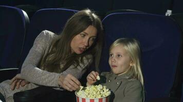 skön kvinna och henne liten dotter äter popcorn tittar på film på de bio video