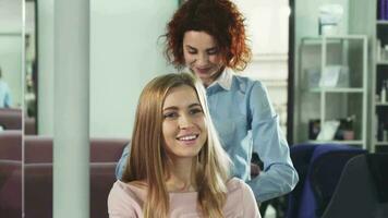 Happy young woman getting her hair combed by professional hairdresser at the salon video