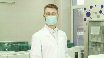 A serious lab assistant stands in the middle of the laboratory and turns his head into the camera video