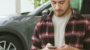 gebaard knap jong Mens gebruik makend van slim telefoon terwijl buying nieuw auto Bij de handel video