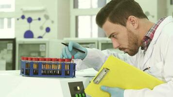 een jong laboratorium assistent duurt uit test buizen met analyses en herschrijft gegevens over hen video