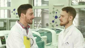Two young lab technicians stand in the middle of the laboratory and talk video
