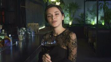 aantrekkelijk jong vrouw zittend Bij de bar glimlachen naar de camera met een glas van wijn in haar hand- video