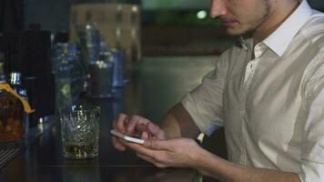 beskurna stänga upp av en man använder sig av hans smart telefon på de bar medan har en dryck video