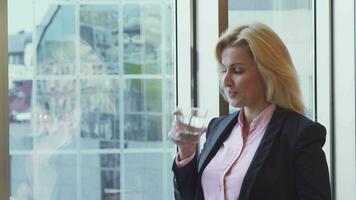 Beautiful woman looks through the window of her office and drinks water video